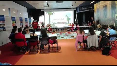 Aula llena de alumnos sentados en mesas frente a la pantalla del reto final de Ciberlandia 21-22, con los instructores al frente.